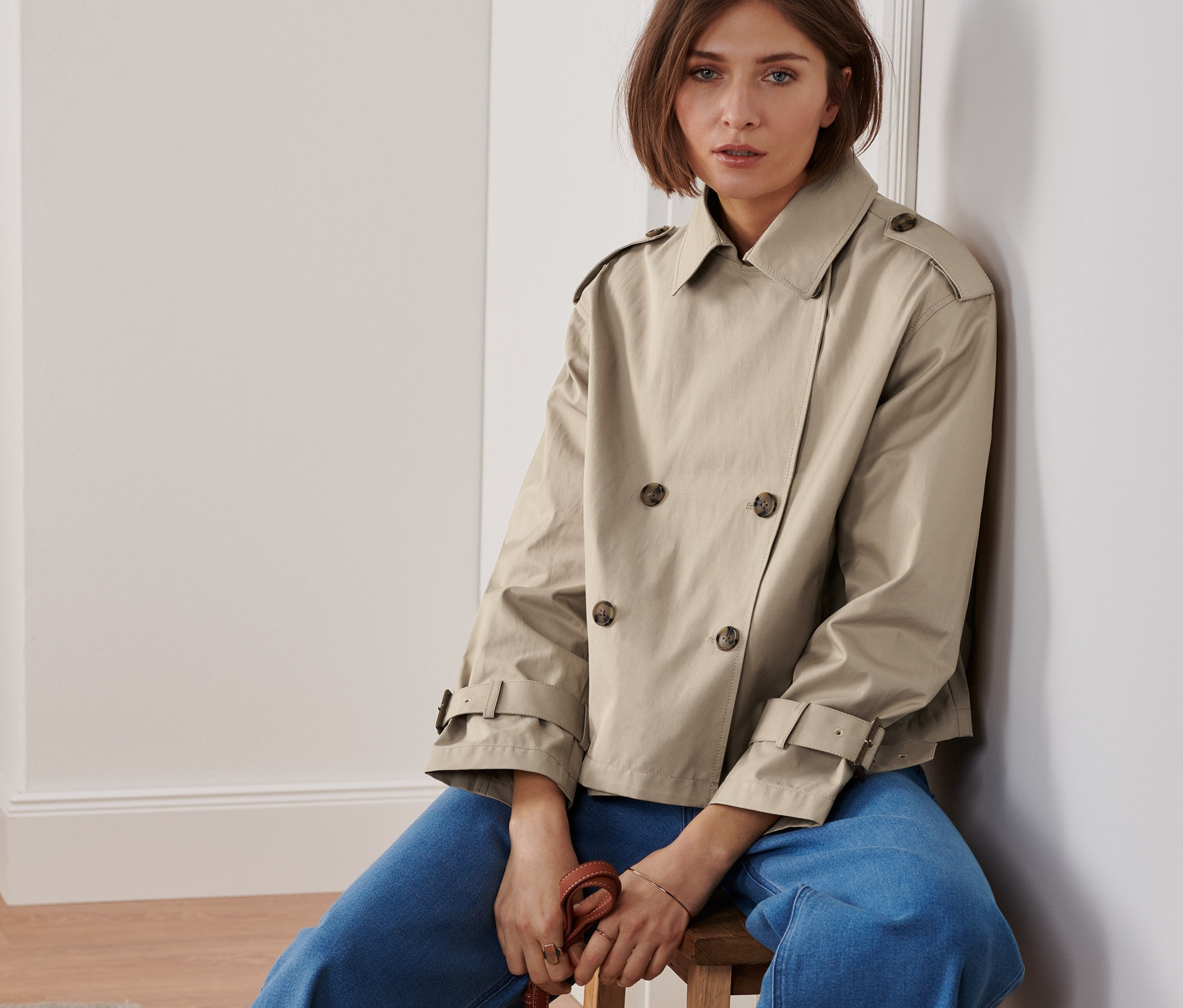 Nő ül egy széken rövid ballonkabátban, barna kézitáskát tartva.