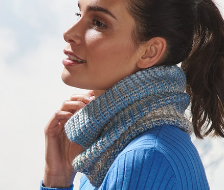 Pulóvert és kötött csősálat viselő nő néz ki.