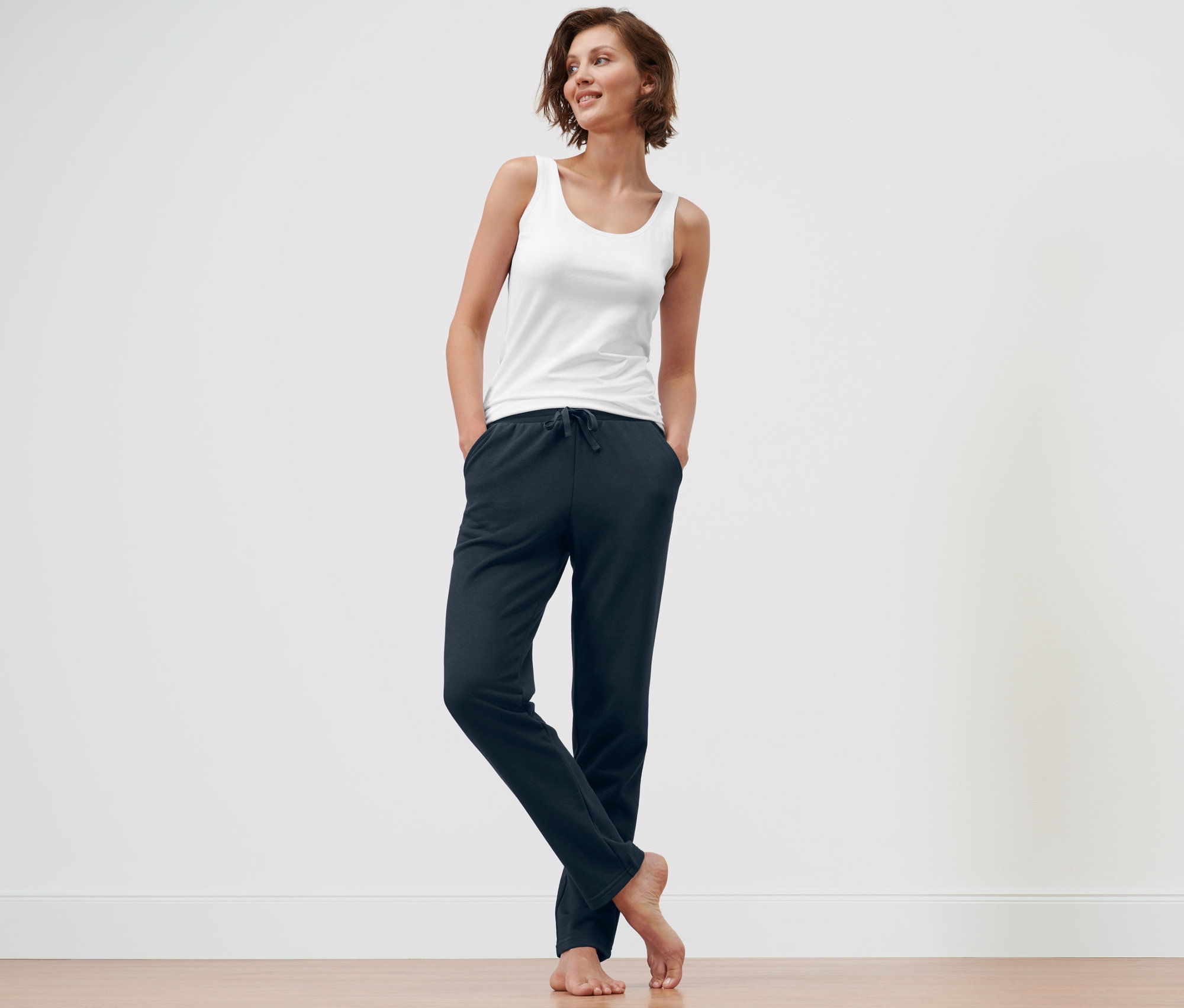 Nő áll sötétkék női szabadidőnadrág és sötétkék női szabadidőnadrág zsebében tartva a kezét.