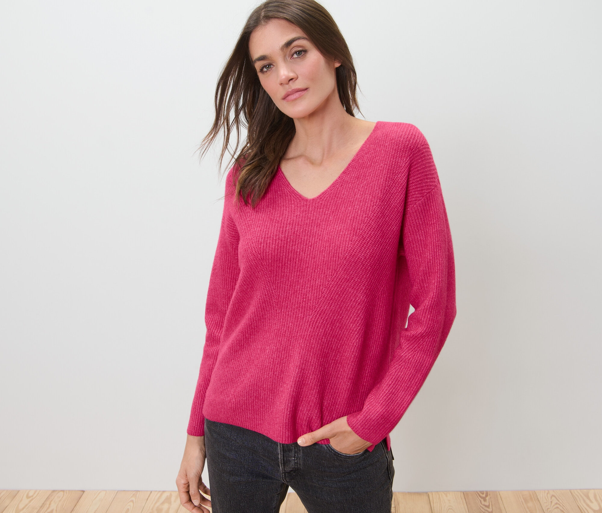 Nő pózol málnaszínű, laza kötésű pulóverben.