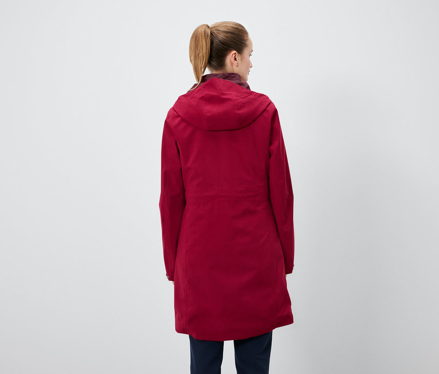 Hátulról látható egy lófarokba kötött hajú nő, aki piros kapucnis kabátot és sötétkék nadrágot visel.