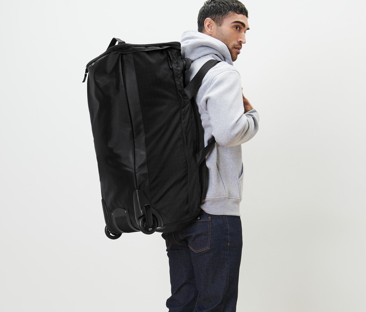 Férfi hátán fekete gurulós utazótáska.