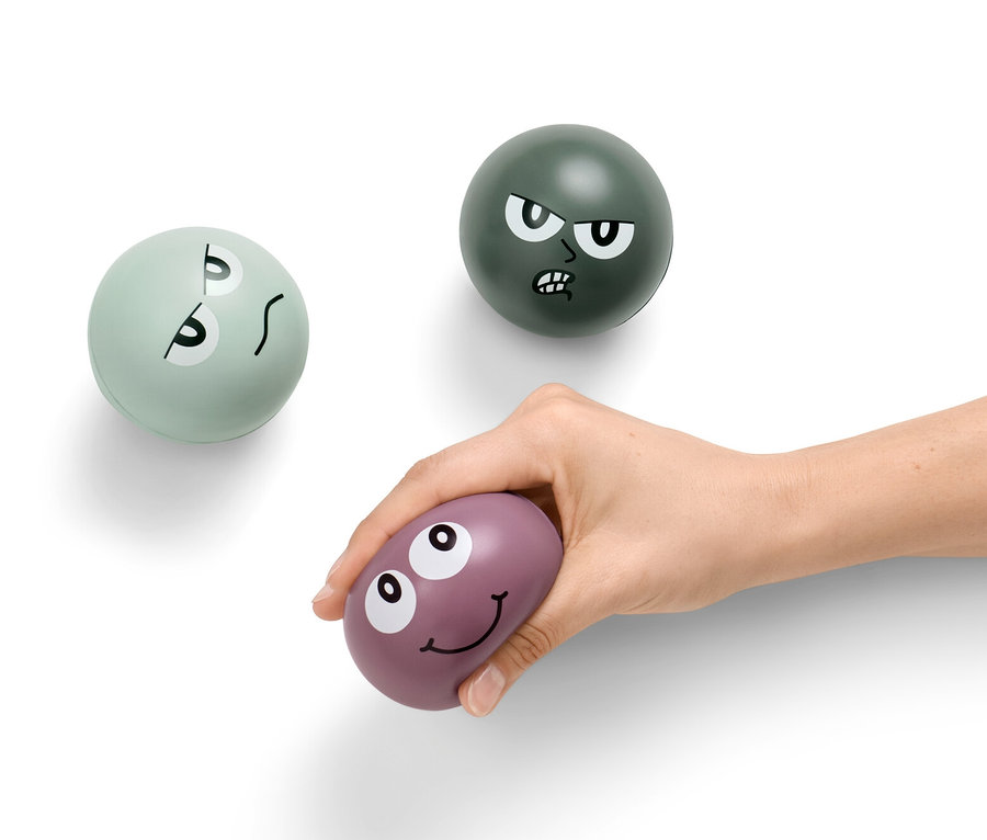 Egy kéz egy lila stresszoldó labdát tart, a háttérben még két stresszoldó labda látható.
