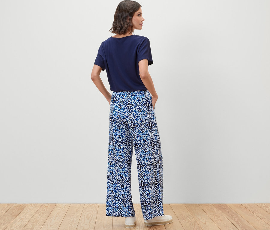 Egy nő áll háttal, kék, mintás, bő szárú nadrágot visel.
