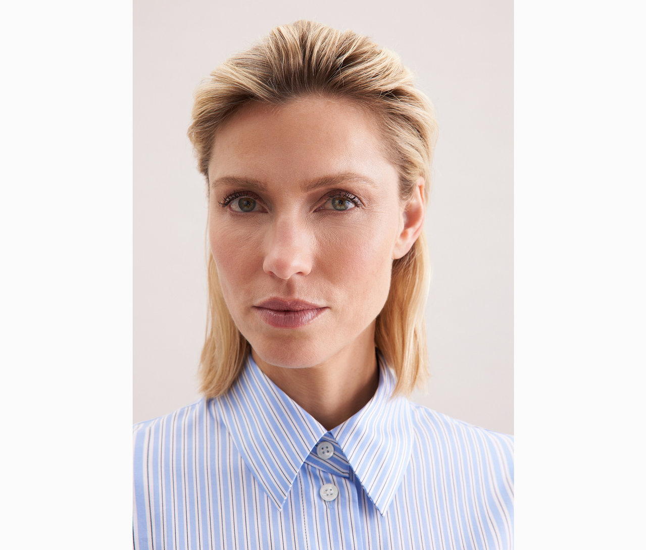Egy szőke hajú nő közeli képe kék-fehér csíkos Seidensticker túlméretezett ingblúzban.