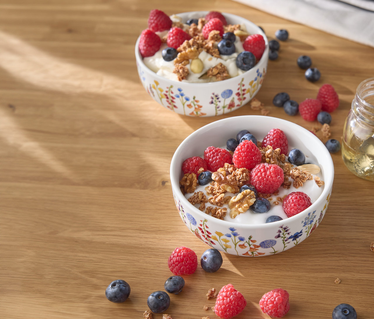 Két tál joghurt málnával, áfonyával és dióval egy fa asztalon.