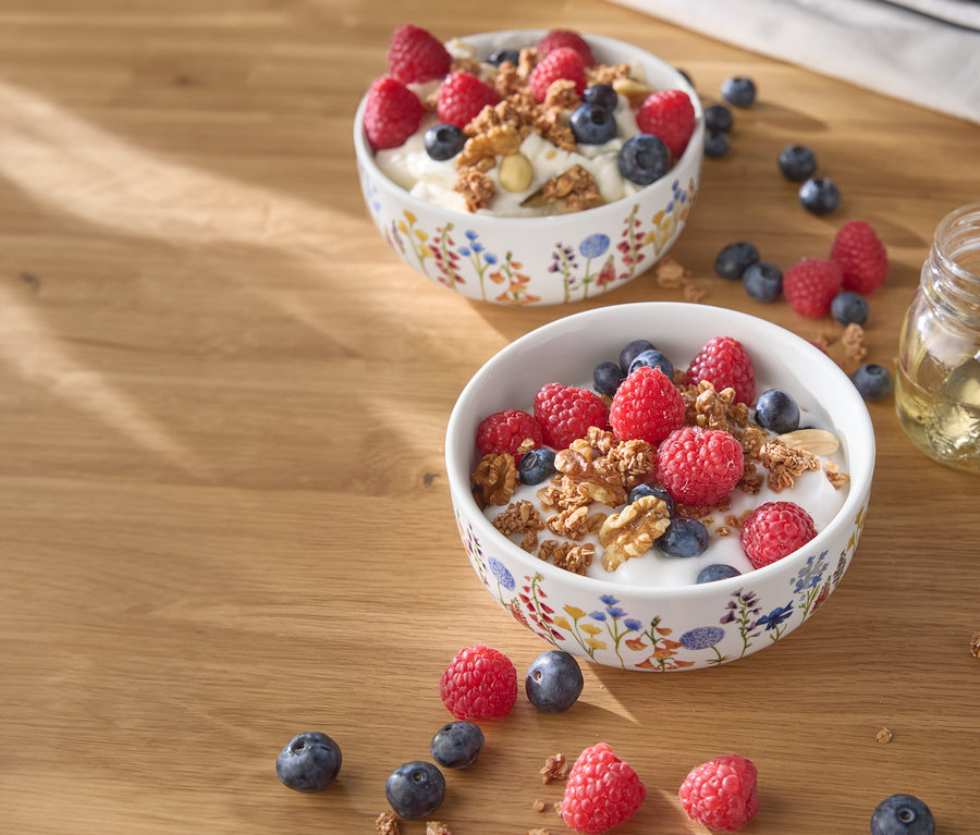 Két tál joghurt málnával, áfonyával és dióval egy fa asztalon.