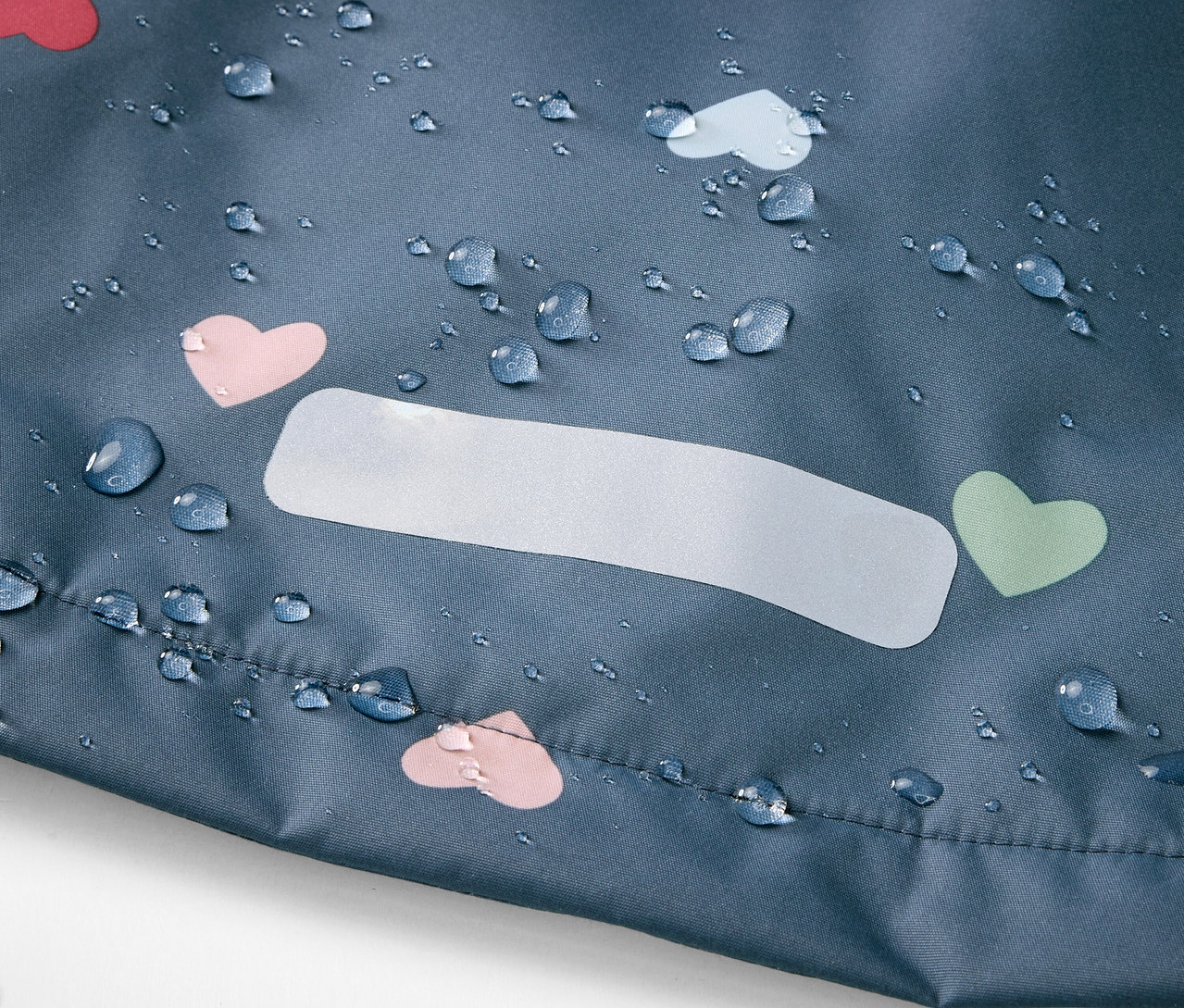 Közelkép egy szívecskemintás gyerek termo esőkabátról vízcseppekkel.