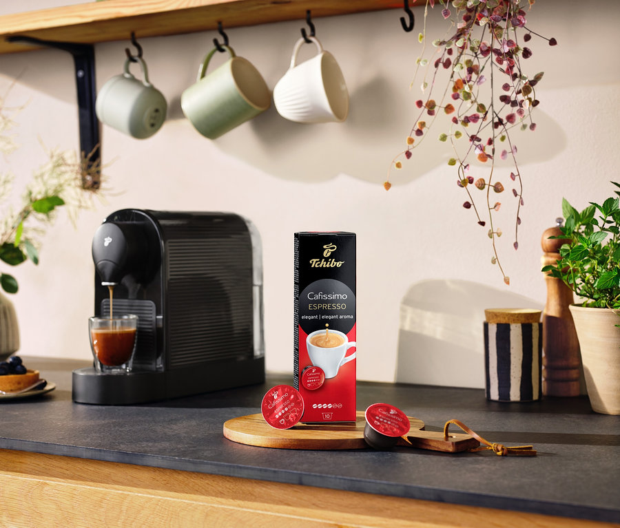 Eszpresszógép kávét tölt egy pohárba egy csomag Cafissimo Espresso elegant – 10 db kávékapszula mellett.