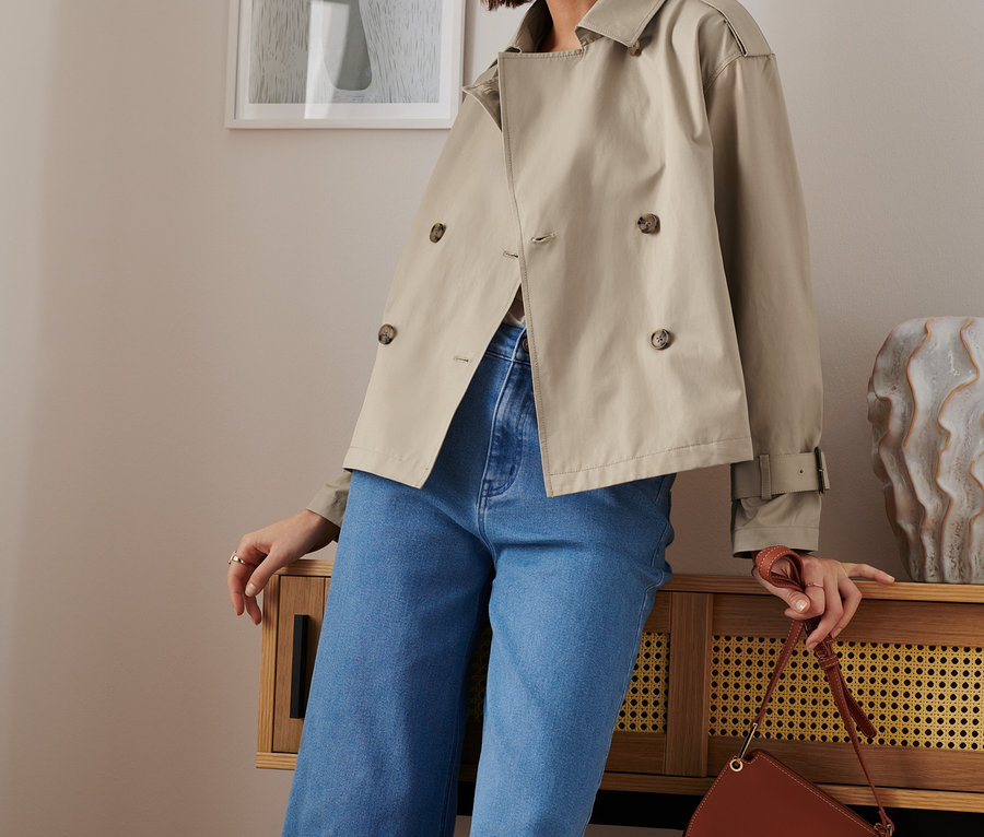 Nő pózol rövid, bézs ballonkabátban.