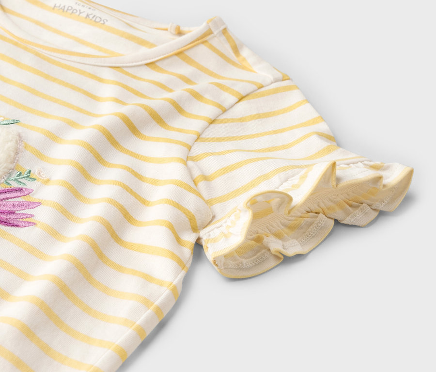 Egy sárga-fehér csíkos, rövid ujjú póló részlete lila virágmintával.