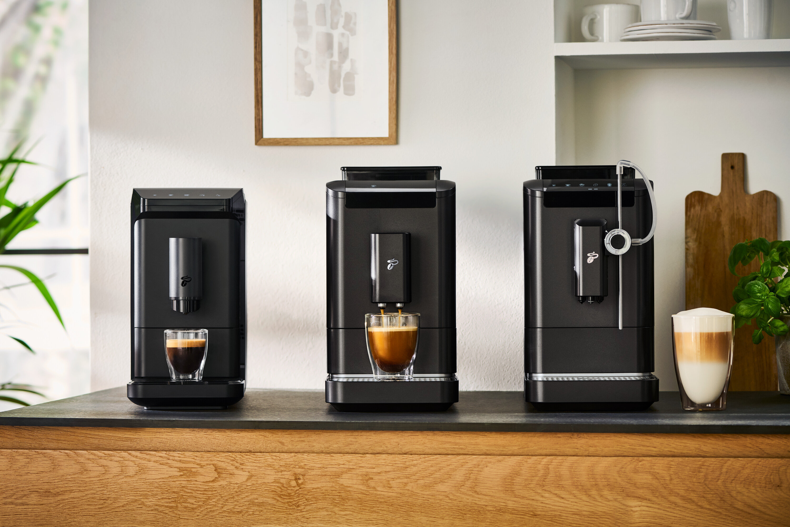 Három kávéfőzőgép áll a pulton, a középsőből kávé folyik egy pohárba, a jobb oldali mellett egy pohár latte macchiato áll.