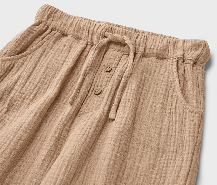 Közelkép egy húzózsinóros és gombos, gyerekmuslinnadrágról.