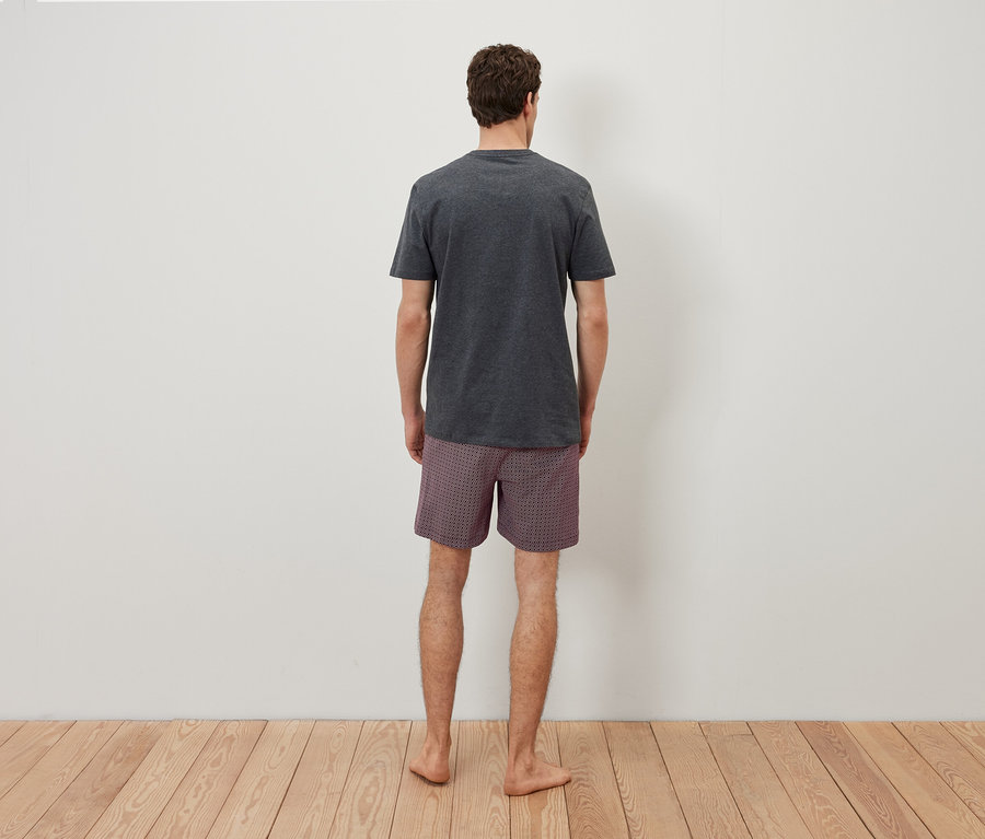 Háttal a kamerának egy férfi szürke pólót és kockás rövidnadrágot visel.