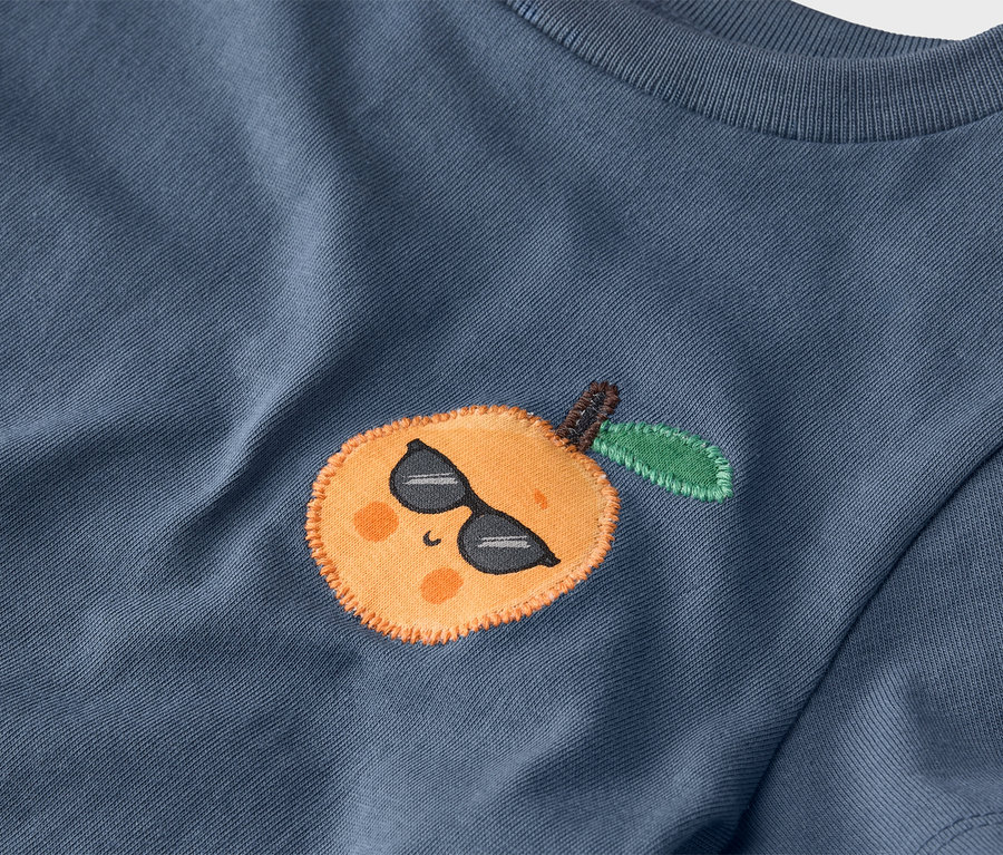 Kék póló közeli képe, narancs hímzéssel, napszemüvegben.