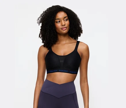Nő visel egy fekete Triaction sportmelltartót és lila leggingset.