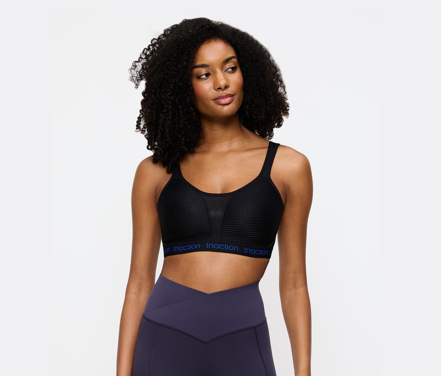 Nő visel egy fekete Triaction sportmelltartót és lila leggingset.