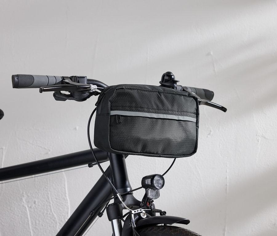 Egy fekete kerékpár részletes képe fekete kormánytáskával és kerékpárlámpával, fehér fal előtt.