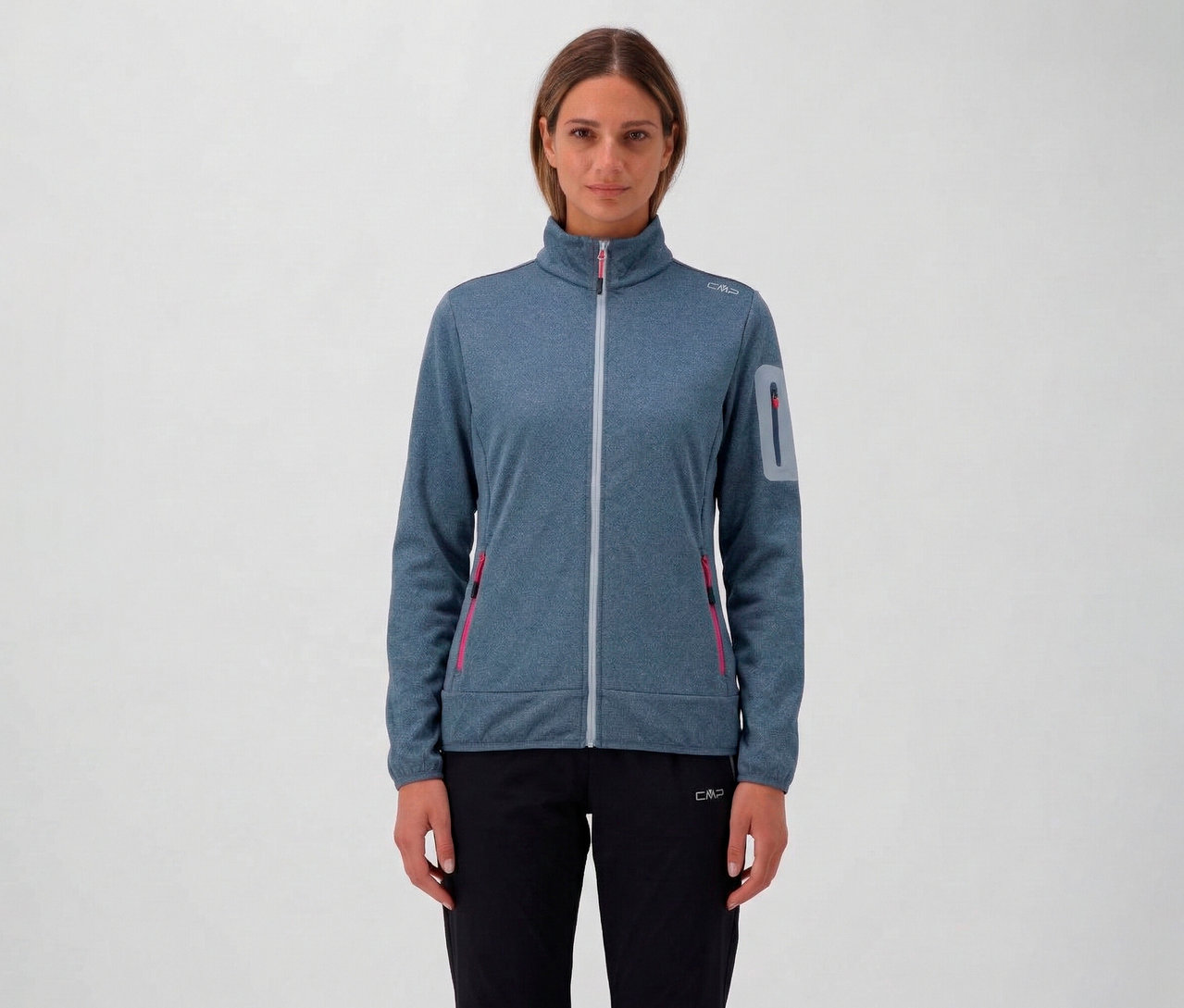 Nő visel kék, melírozott CMP női dzsekit cipzárral és fekete nadrágot semleges háttér előtt.