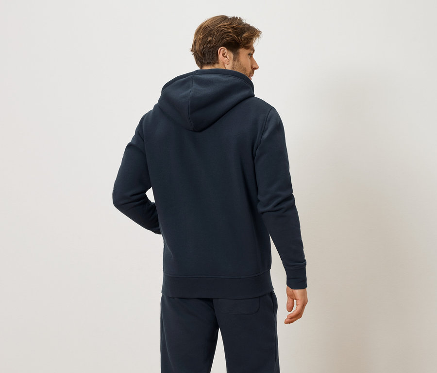 Hátulnézet egy barna hajú férfiról, aki sötétkék kapucnis pulóvert és sötétkék melegítőnadrágot visel.