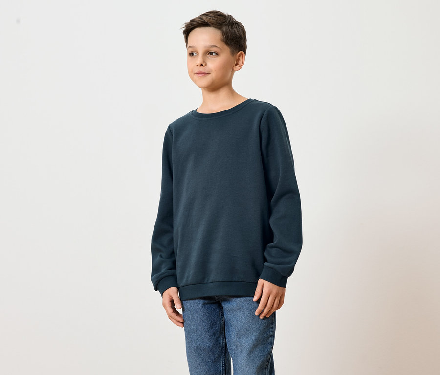 Egy fiatalember sötétkék pulóvert és farmert visel.