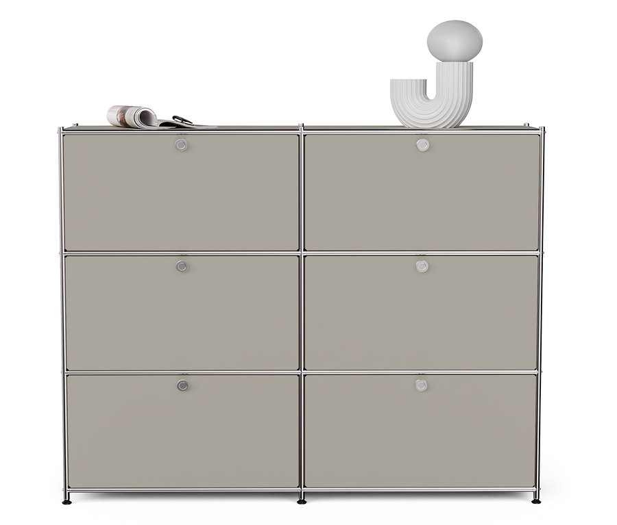 Világosszürke »CN3« fém komód hat lenyíló ajtóval. Az ajtókon újság és egy fehér dekoráció látható.