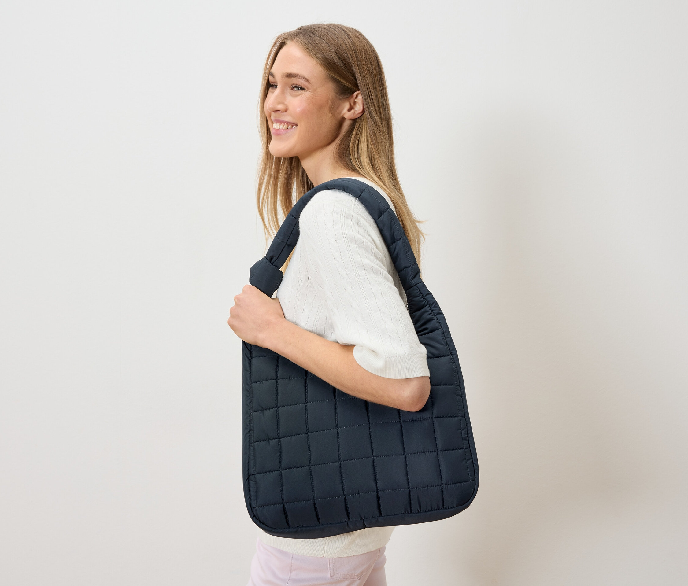 Nő visz a vállán egy sötétkék, steppelt táskát.