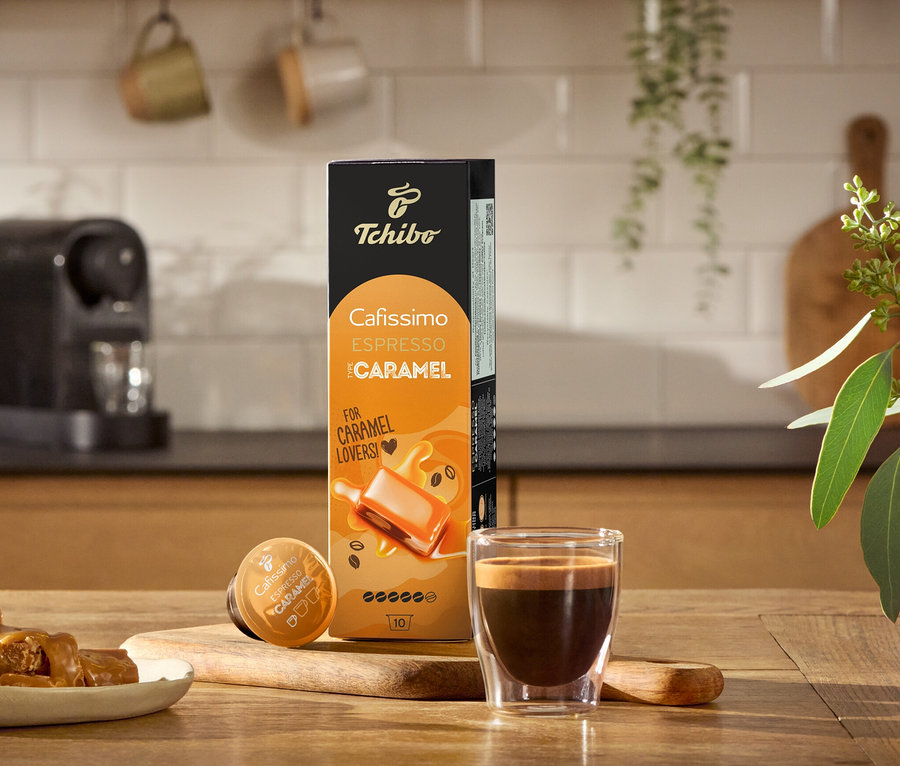 Eszpresszó, karamellás cukorkák és egy Cafissimo Flavoured Edition - Espresso Caramel - 80 db-os kávékapszula csomagolás egy fa asztalon.