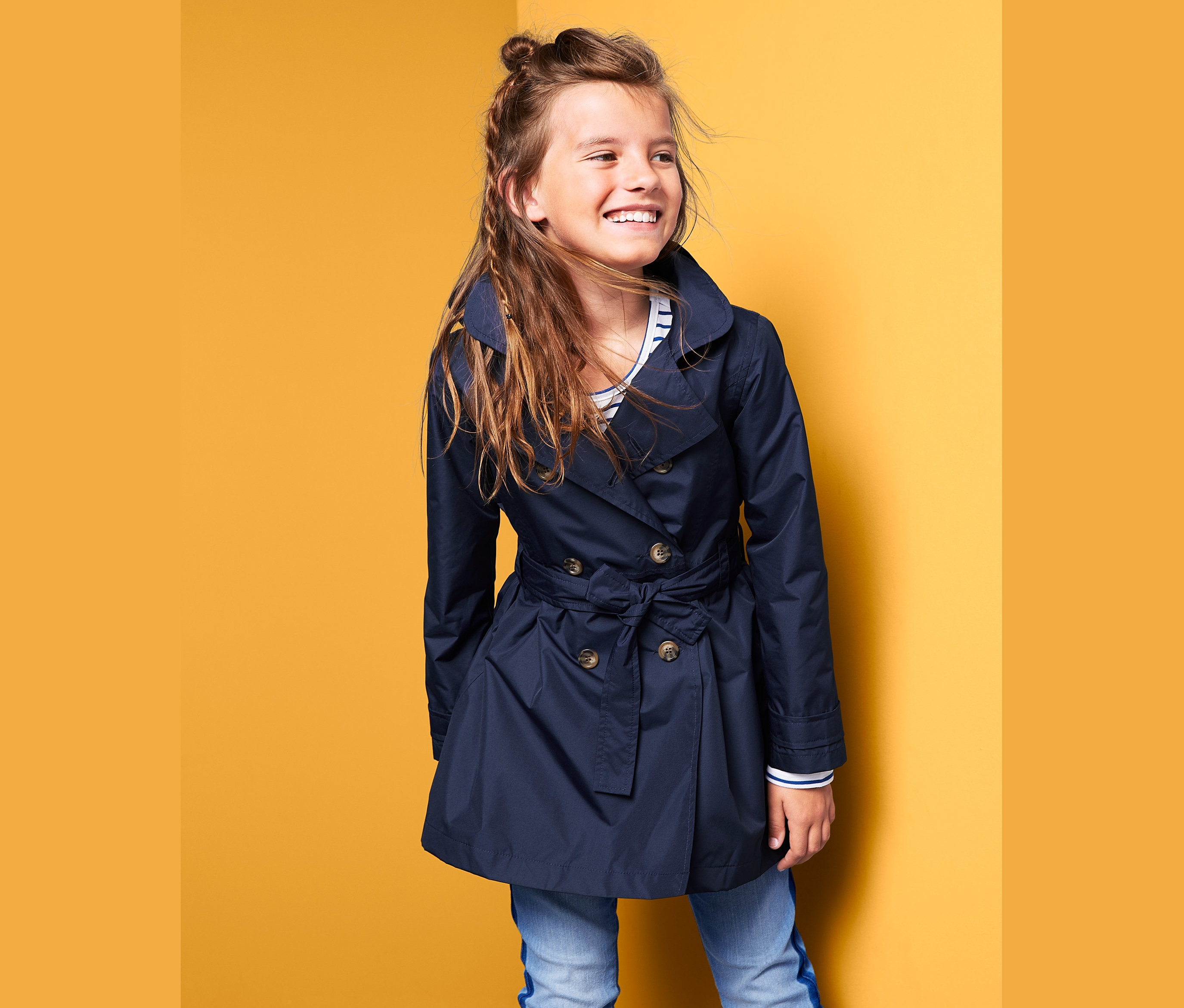 Mosolygó lány sötétkék lány ballonkabátban pózol.