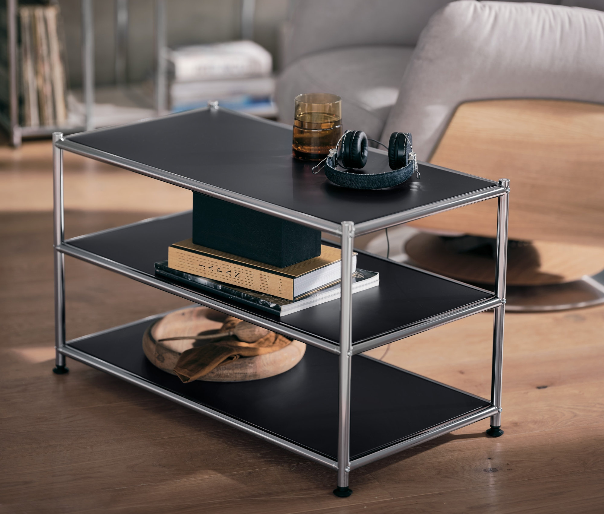 Fekete fém dohányzóasztal, üveg és fejhallgató a felső polcon.