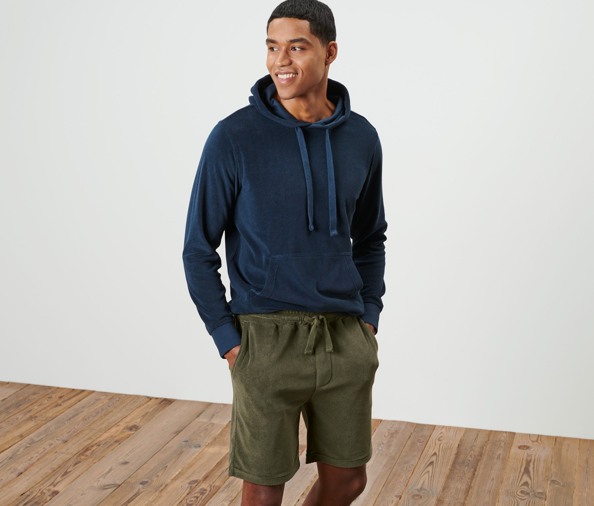 Egy mosolygó férfi áll kék kapucnis pulóverben és zöld frottír rövidnadrágban.