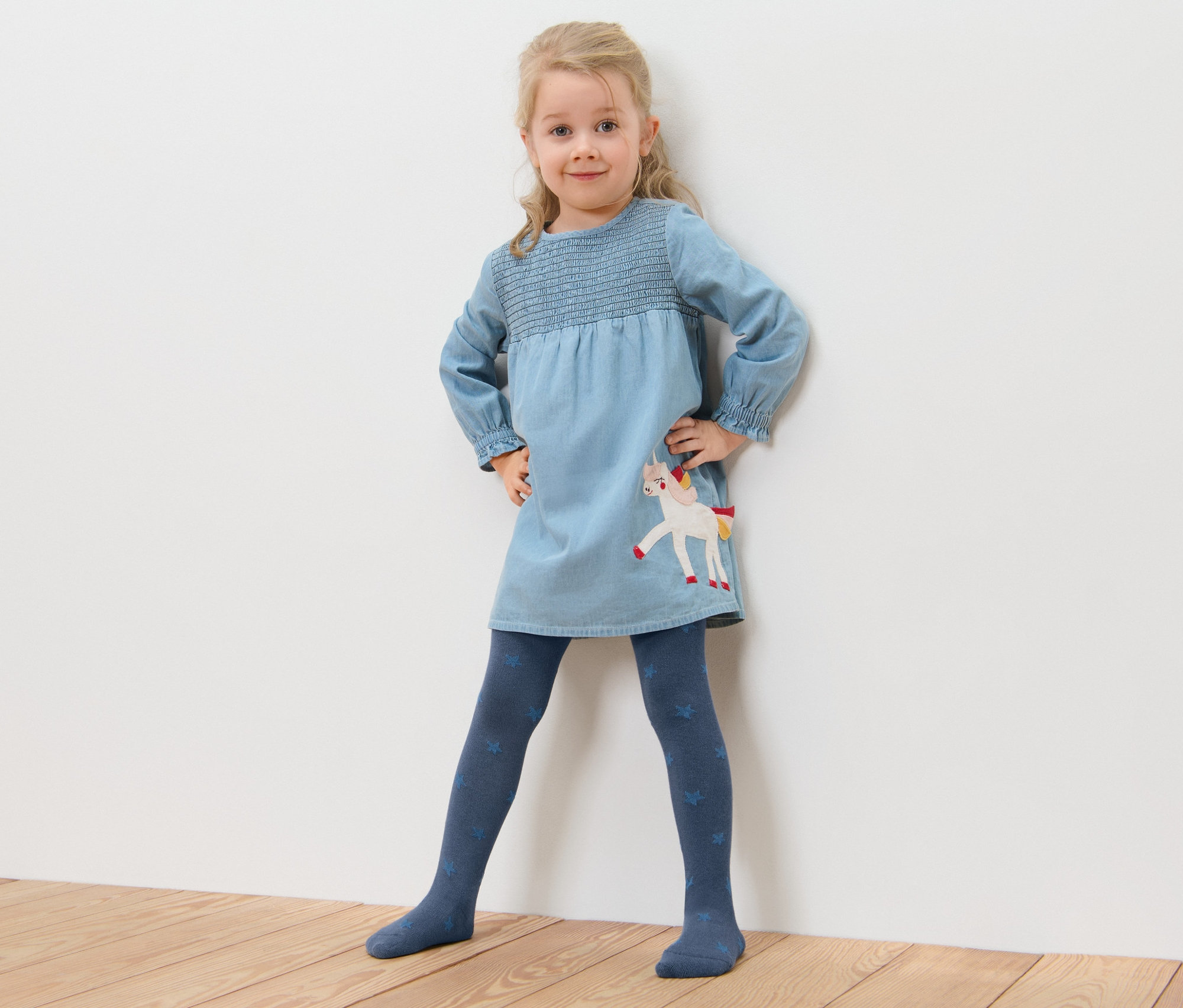 Kislány pózol kék unikornisos ruhában és 5 darab csillagos pamut harisnyanadrágban.