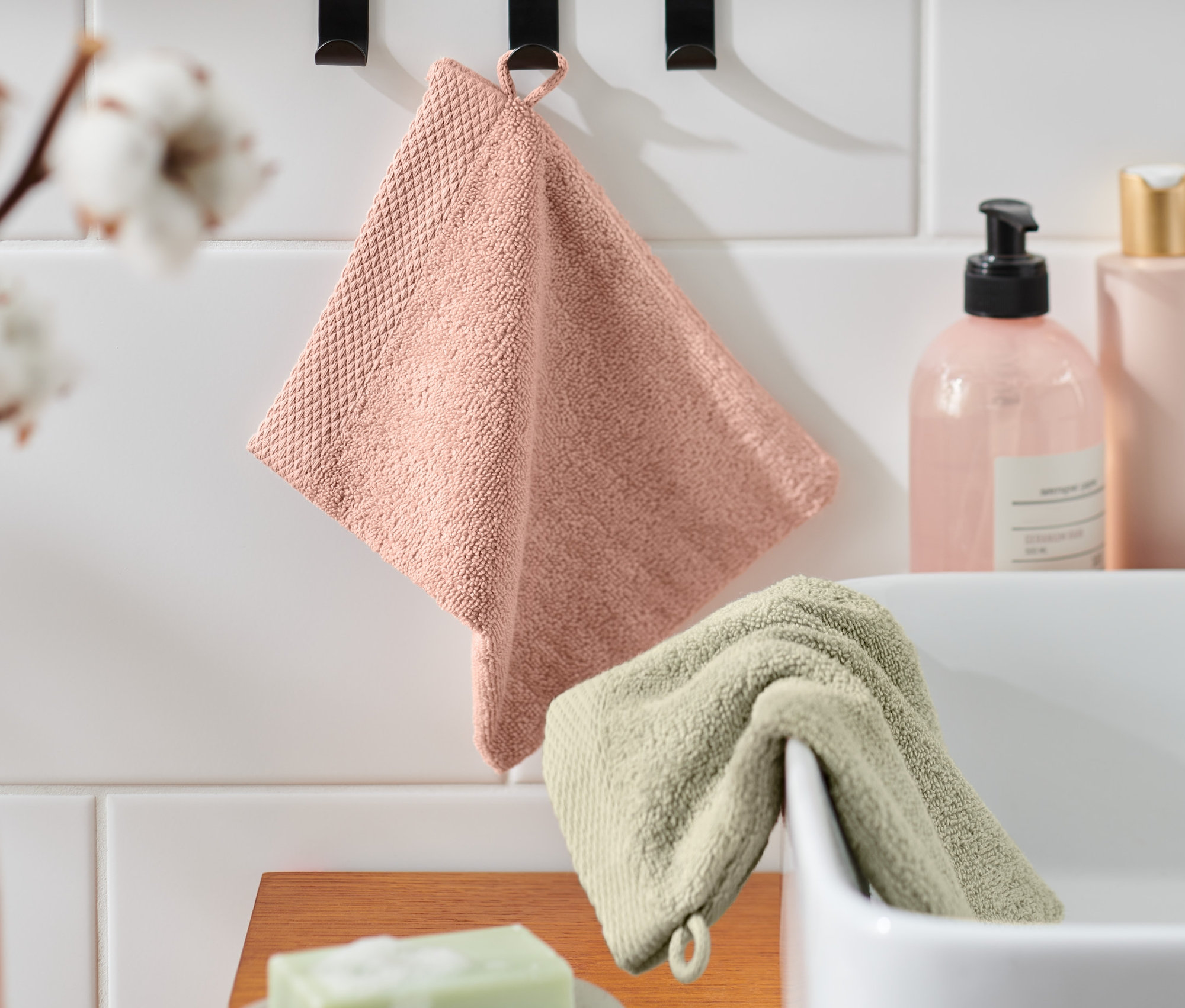 Két kiváló minőségű kozmetikai kesztyű lóg a fürdőszobában, egy rózsaszín és egy zöld.