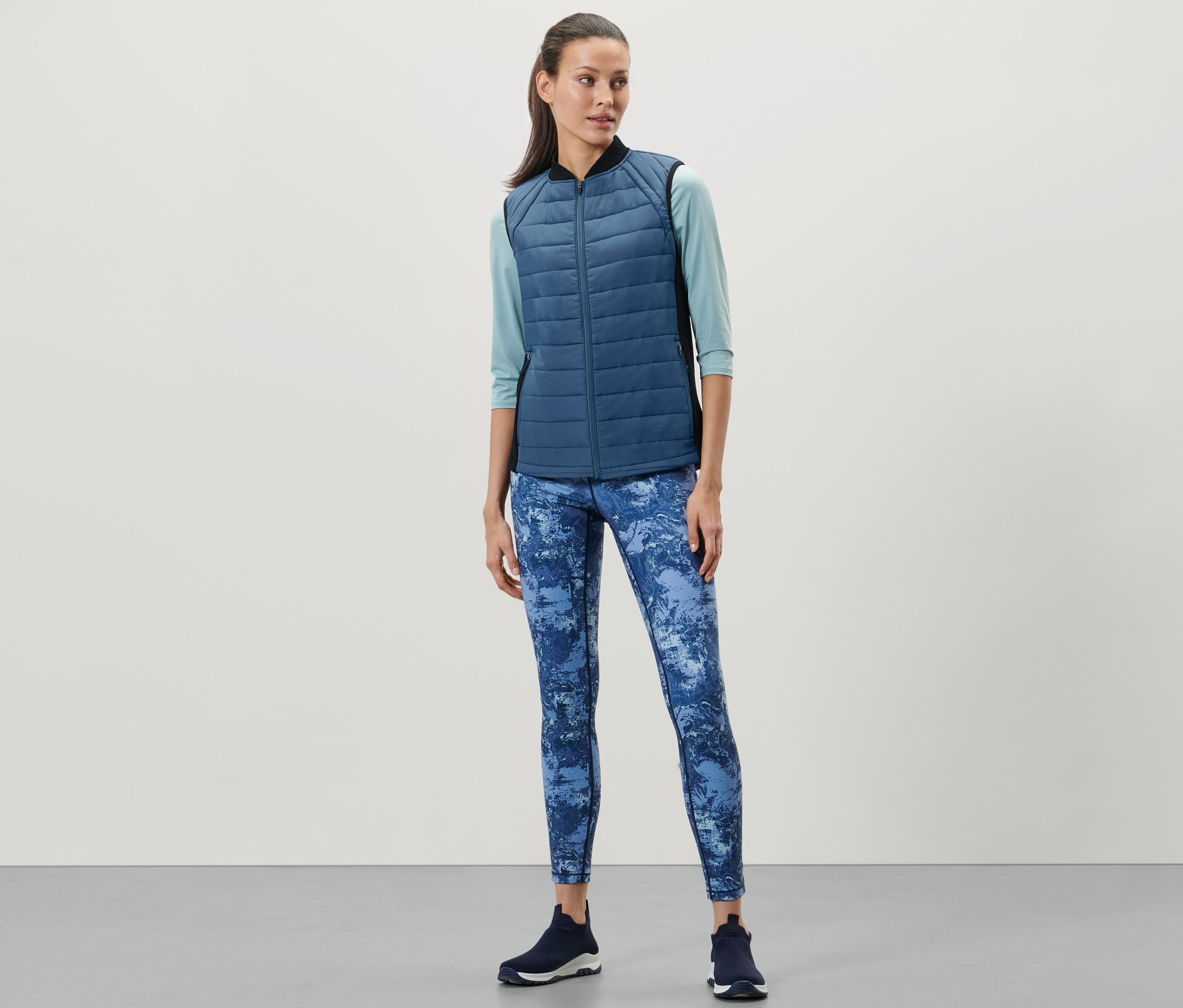 Nő visel kék steppelt termomellényt, kék leggingset és sötét tornacipőt.