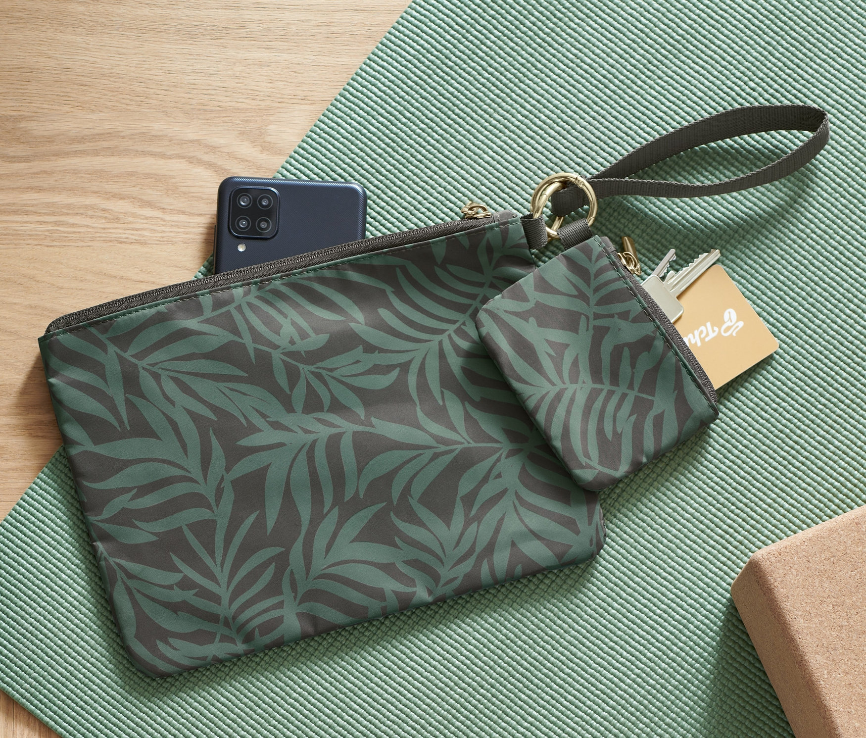 Két levélmintás tárolótáska fekszik egy zöld edzőszőnyegen egy fatömb és egy mobiltelefon mellett.