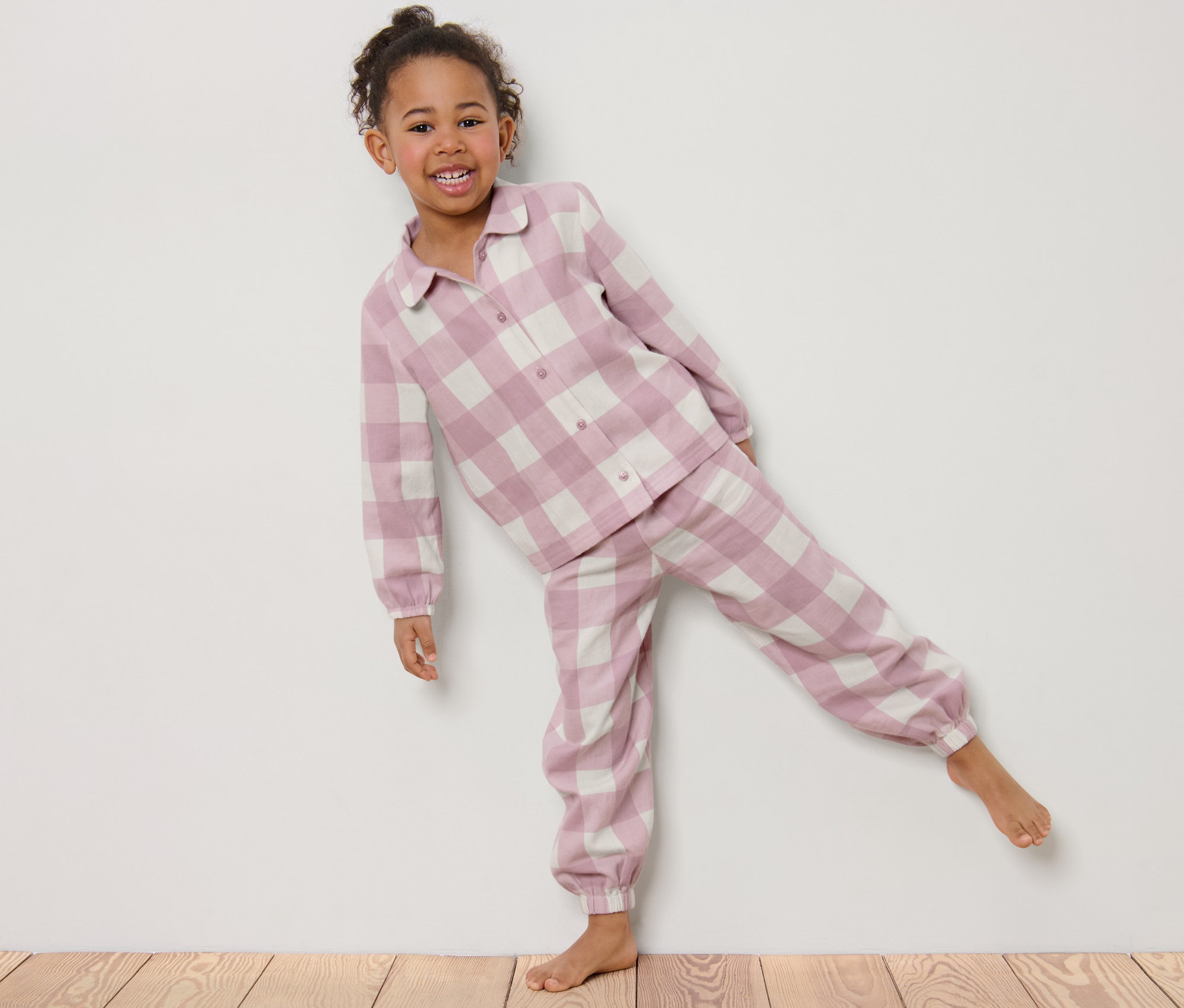 Egy mosolygós kislány kockás mintájú flanel pizsamában pózol.