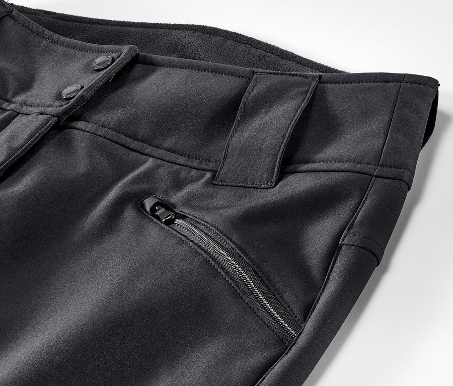 Egy fekete női softshell jet sínadrág részlete, gombos zárással és cipzáras zsebbel.