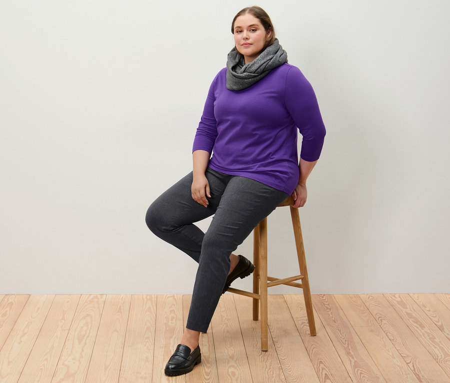 Nő ül egy széken, sztreccsnadrágot és lila, 3/4-es ujjú felsőt visel.