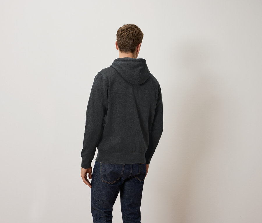 Egy férfi háttal a kamerának, sötétszürke kapucnis pulóvert és farmert visel.