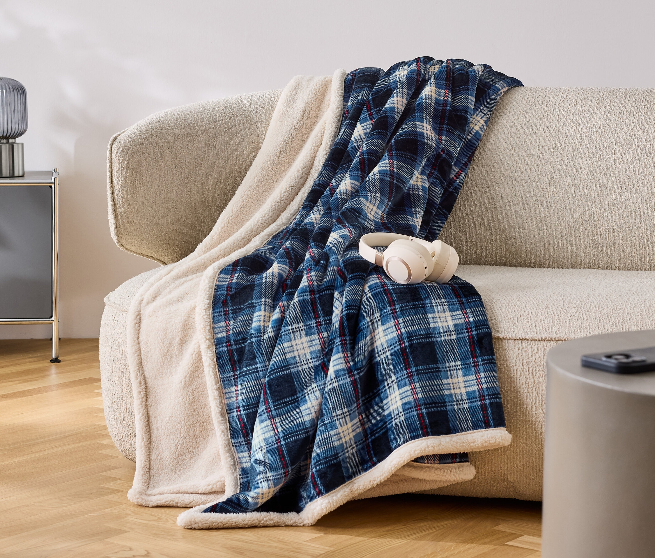 Egy bézs színű kanapén egy kék-fehér kockás takaró van fehér szegéllyel. A takarón fehér fejhallgató található.