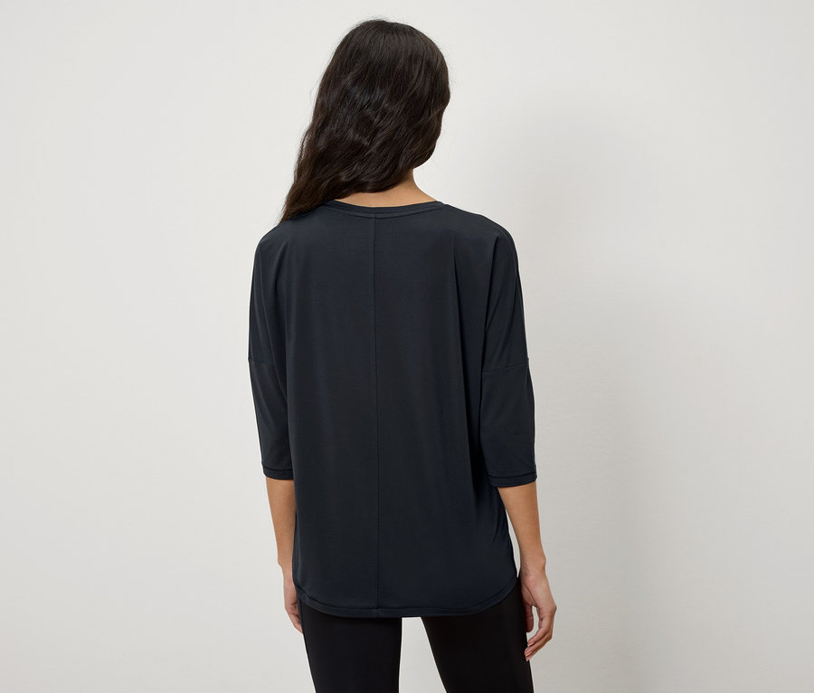 A kamerának háttal álló nő háromnegyedes ujjú, fekete pólót visel.