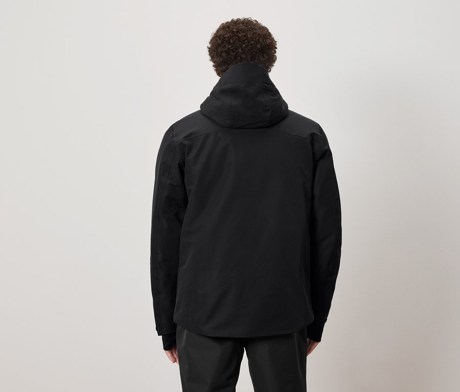 Göndör hajú férfi áll háttal, fekete kapucnis kabátot visel.