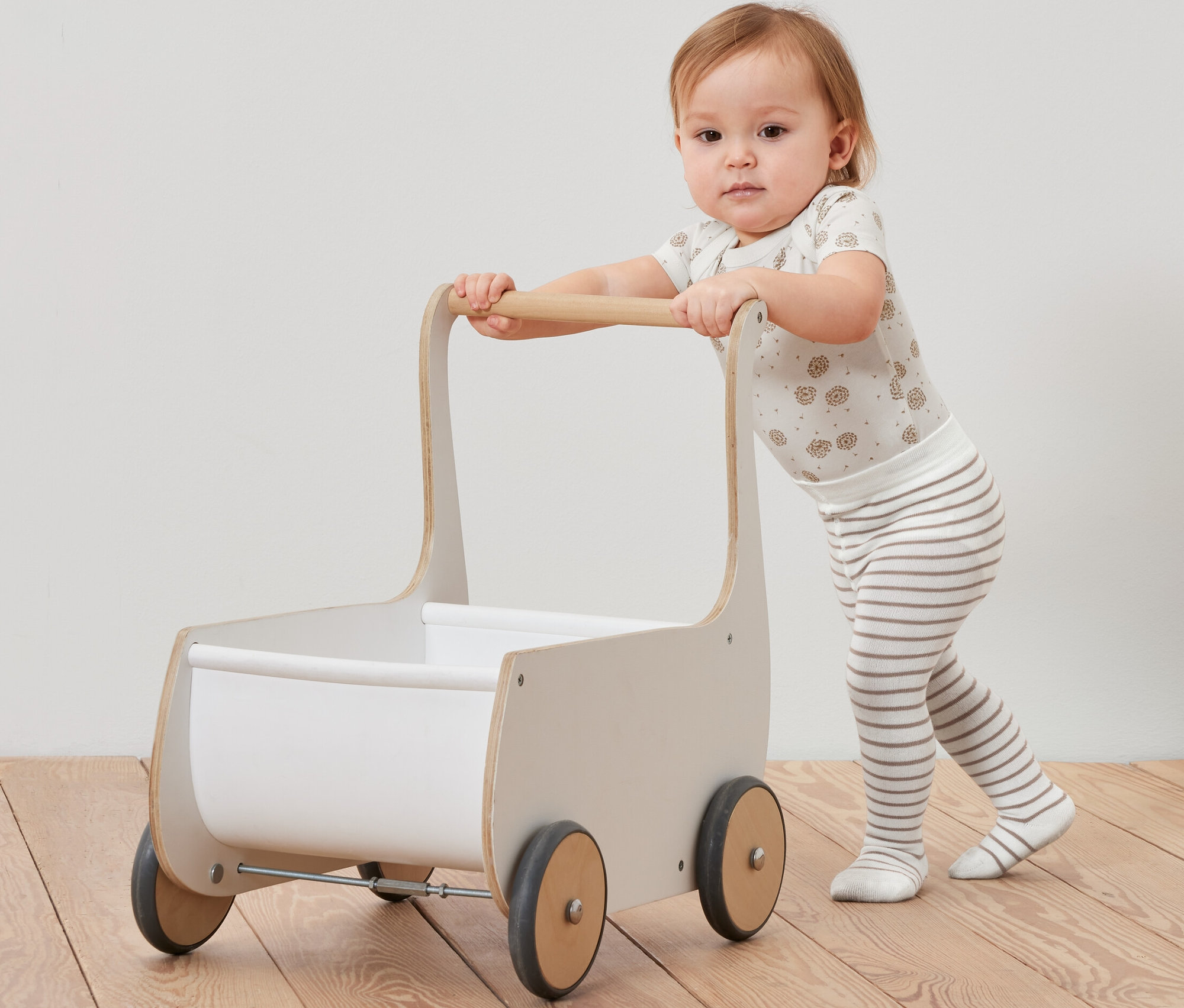 Egy kisgyermek tol egy fából készült kocsit, és a lábán 5 kisgyerek harisnyanadrág van.
