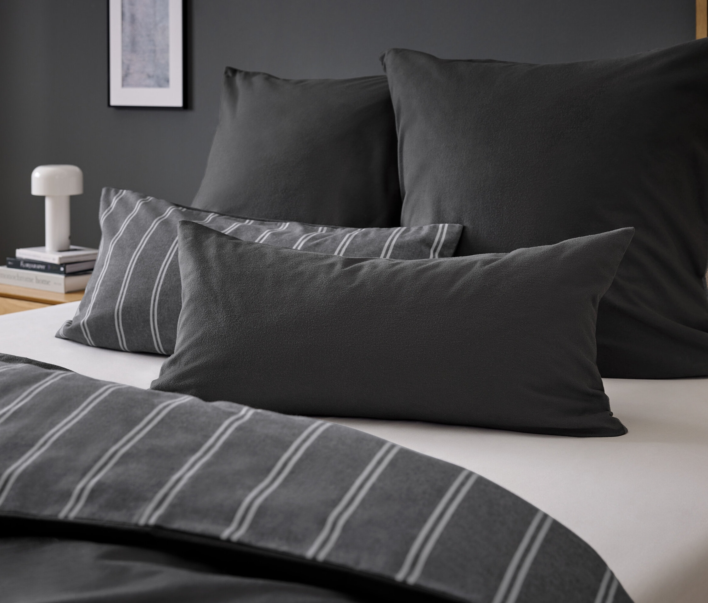 Négy szürke párna egy ágyon szürke csíkos ágyneművel.
