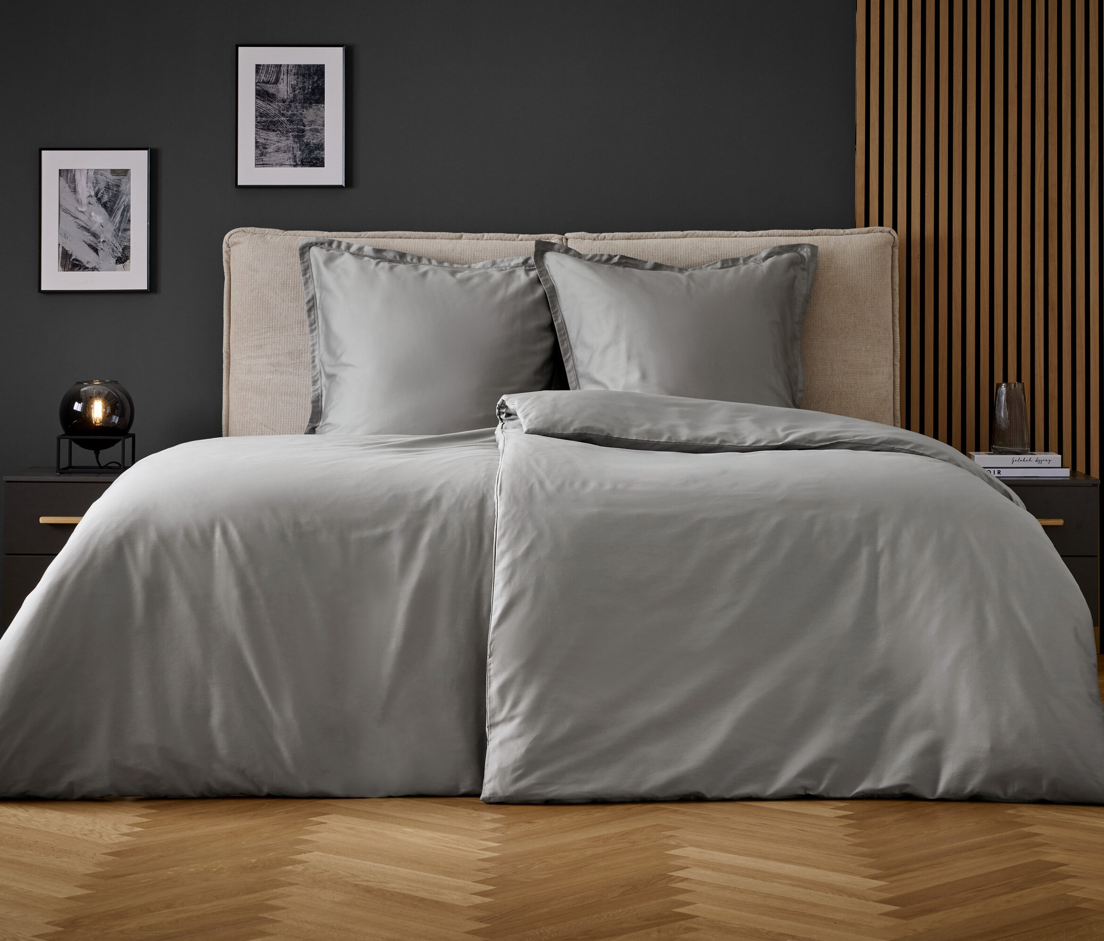 Szürke ágynemű egy ágyon két párnával és éjjeliszekrényekkel az oldalán.