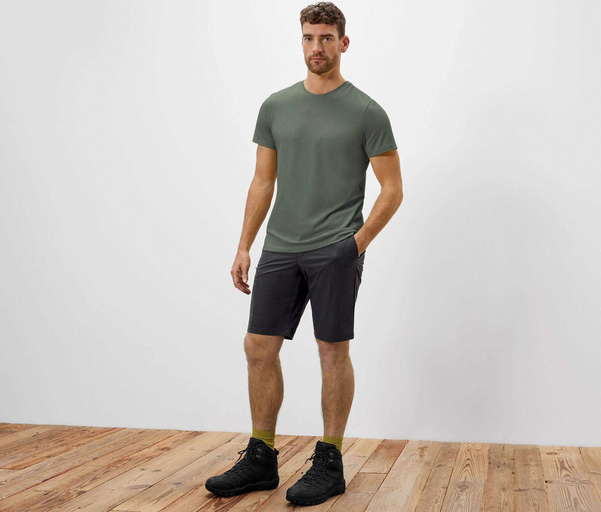 Egy férfi áll, keze a férfi funkcionális softshell rövidnadrág antracit színű zsebében.
