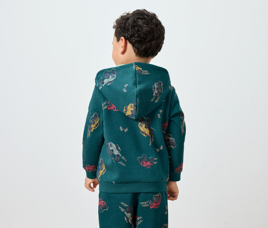 Egy fiú háttal áll, zöld, autómintás kapucnis pulóvert és melegítőnadrágot visel.