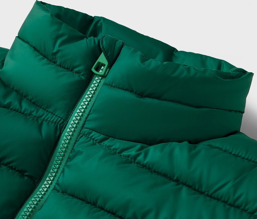 Egy zöld, steppelt dzseki részlete gallérral és cipzárral.