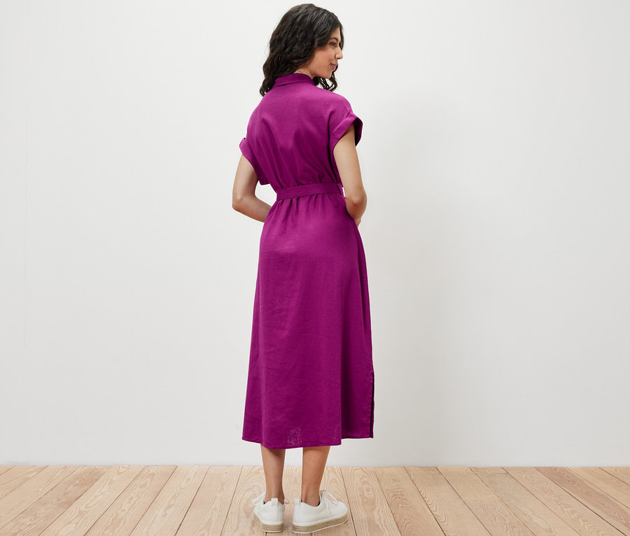 Egy nő háttal áll a kamerának és egy fukszia színű lenvászon blúzruhát visel.