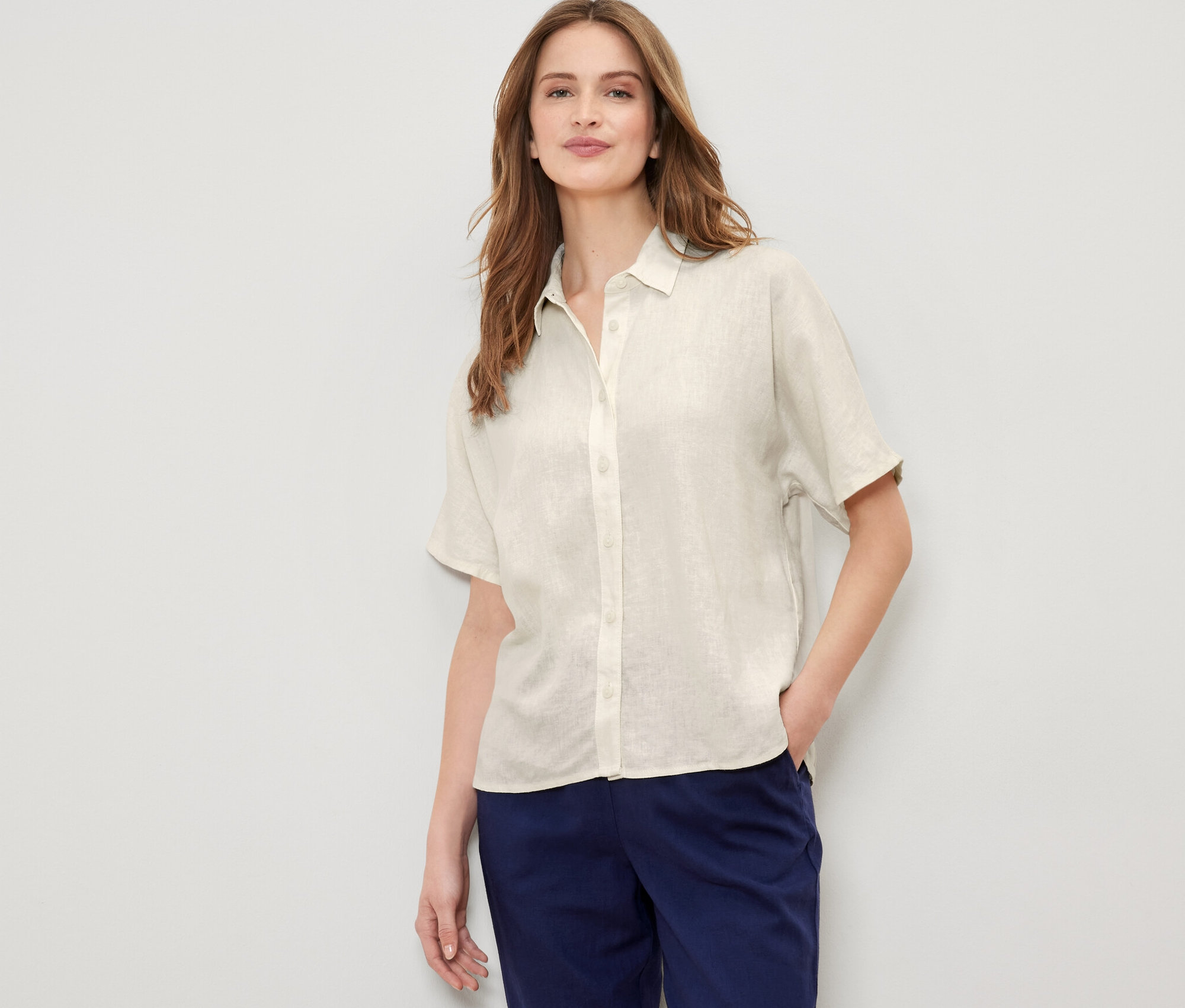 Nő pózol krémszínű lenvászon ingblúzban.